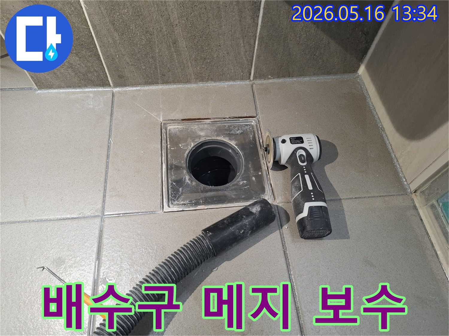 누수 엔지니어가 욕실 배수구 주변의 타일 메지 누수를 해결하기 위해-낡은 메지를 전동 공구로 제거하고-흡입 호스로 현장을 정리하는 중입니다