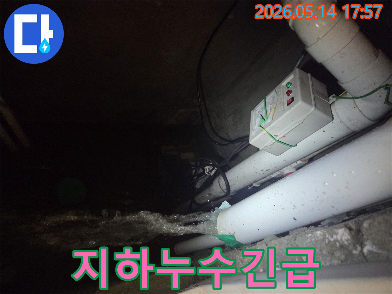 어두운 지하 공간에서-파이프에서 물이 강하게 뿜어져 나오는-긴급 누수 현장을 보여주는 사진입니다-전기 제어 박스와 배관들이 함께 보입니다.
