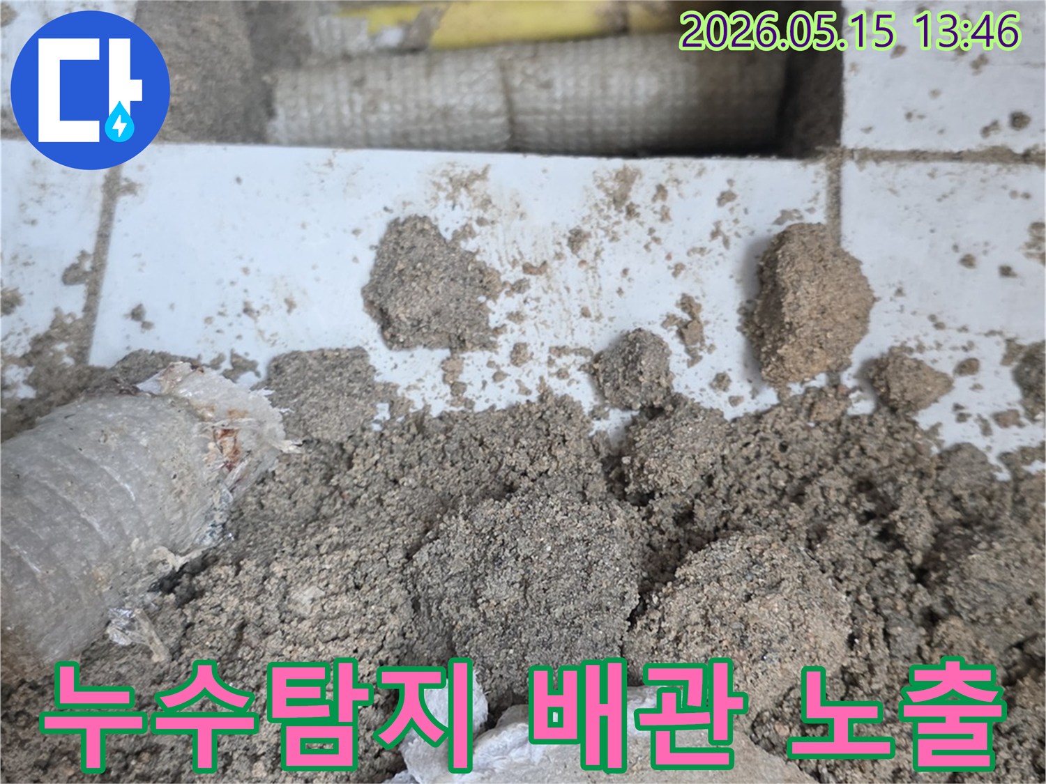 누수 공사 현장에서-바닥을 개방하여-드러난 배관과-주변의 흙더미-그리고-파손된 타일 조각들입니다