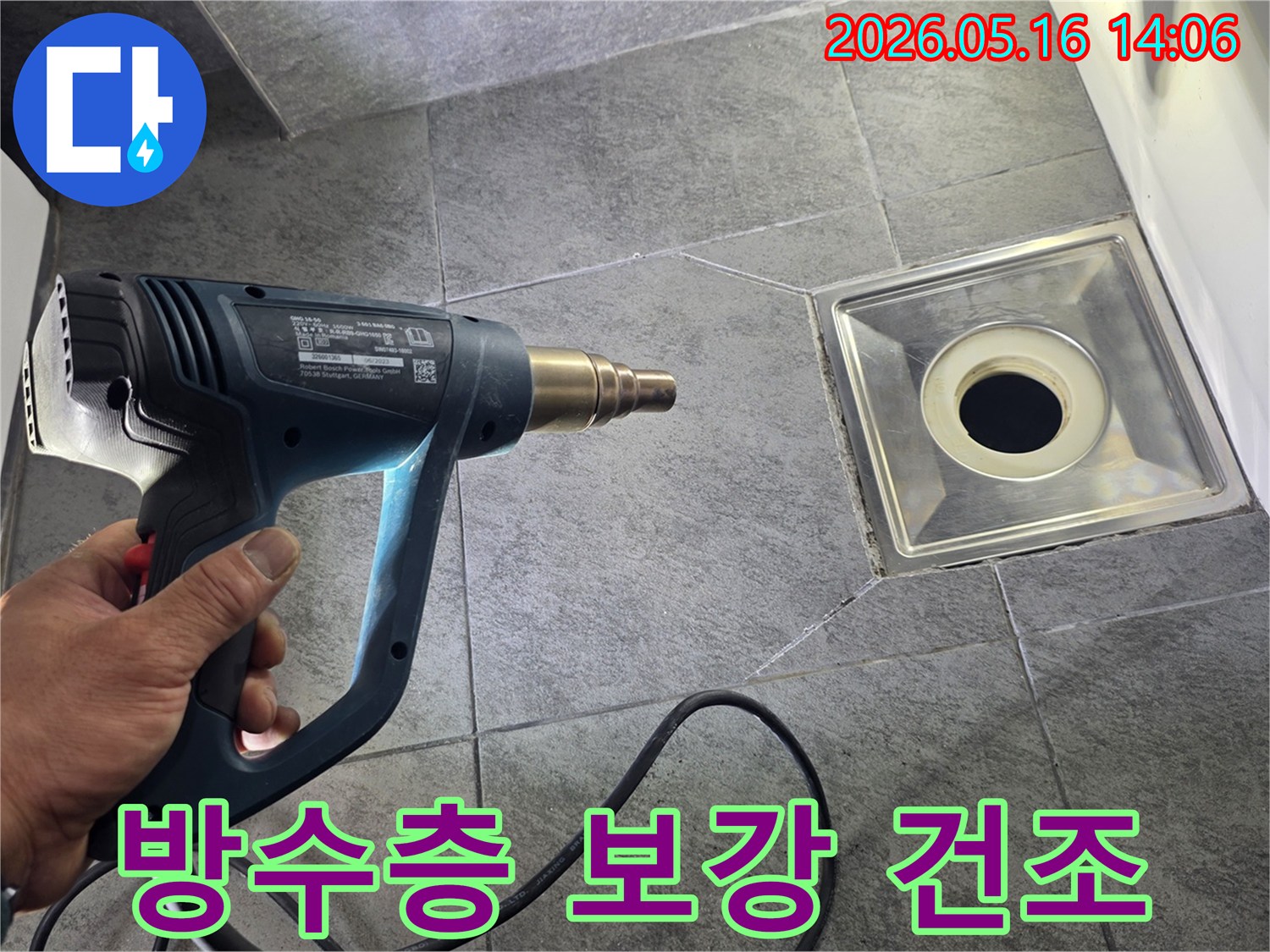 누수 전문가가 욕실 바닥의 배수구 주변을 열풍기로 건조하여-방수층 보강 작업을 준비하는-모습입니다.