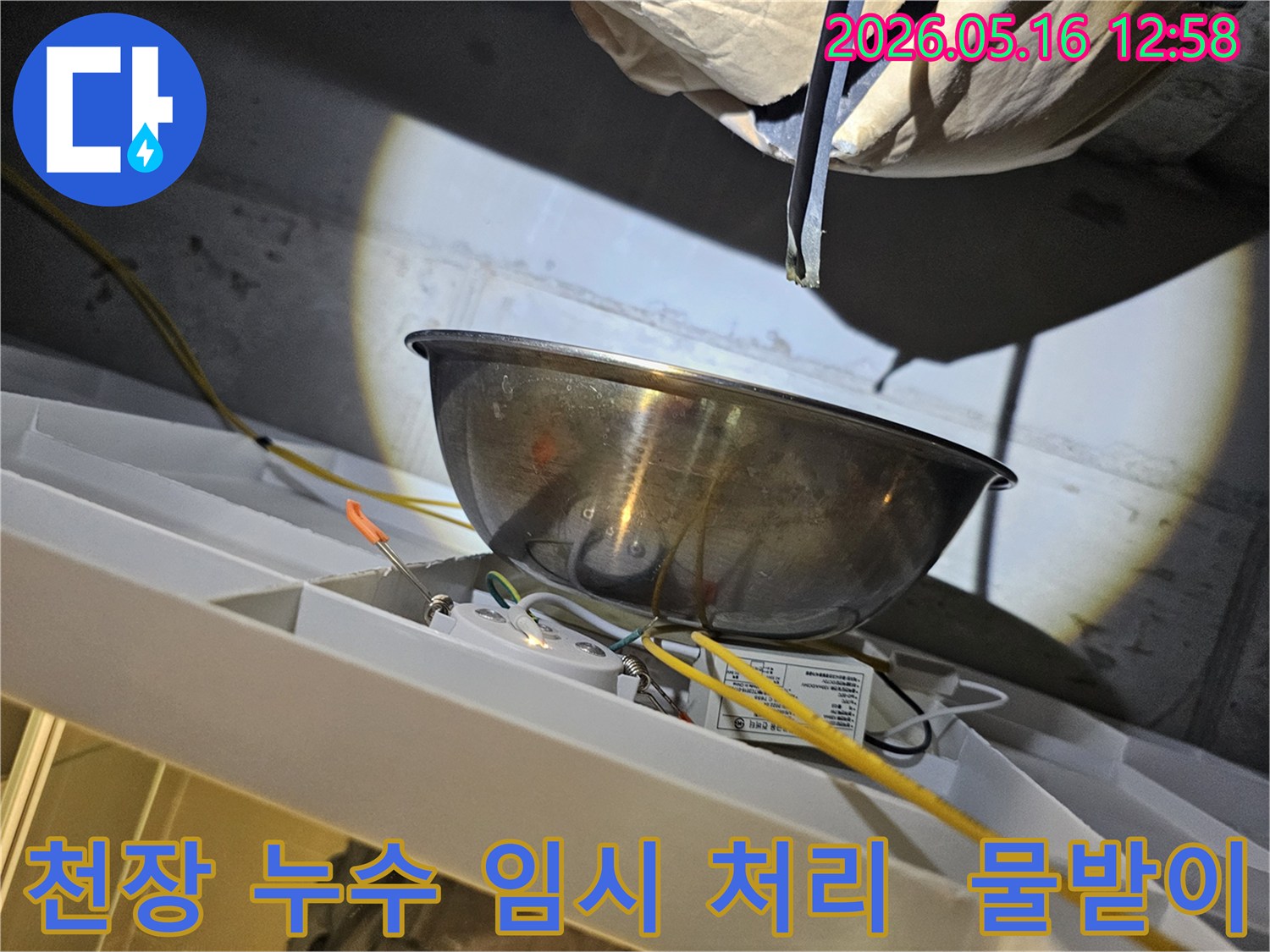 천장에서 물이 새는 것을-스테인리스 그릇으로-받아내며-전기 배선과-조명 장치 주변의-안전 상태를-점검하는 모습