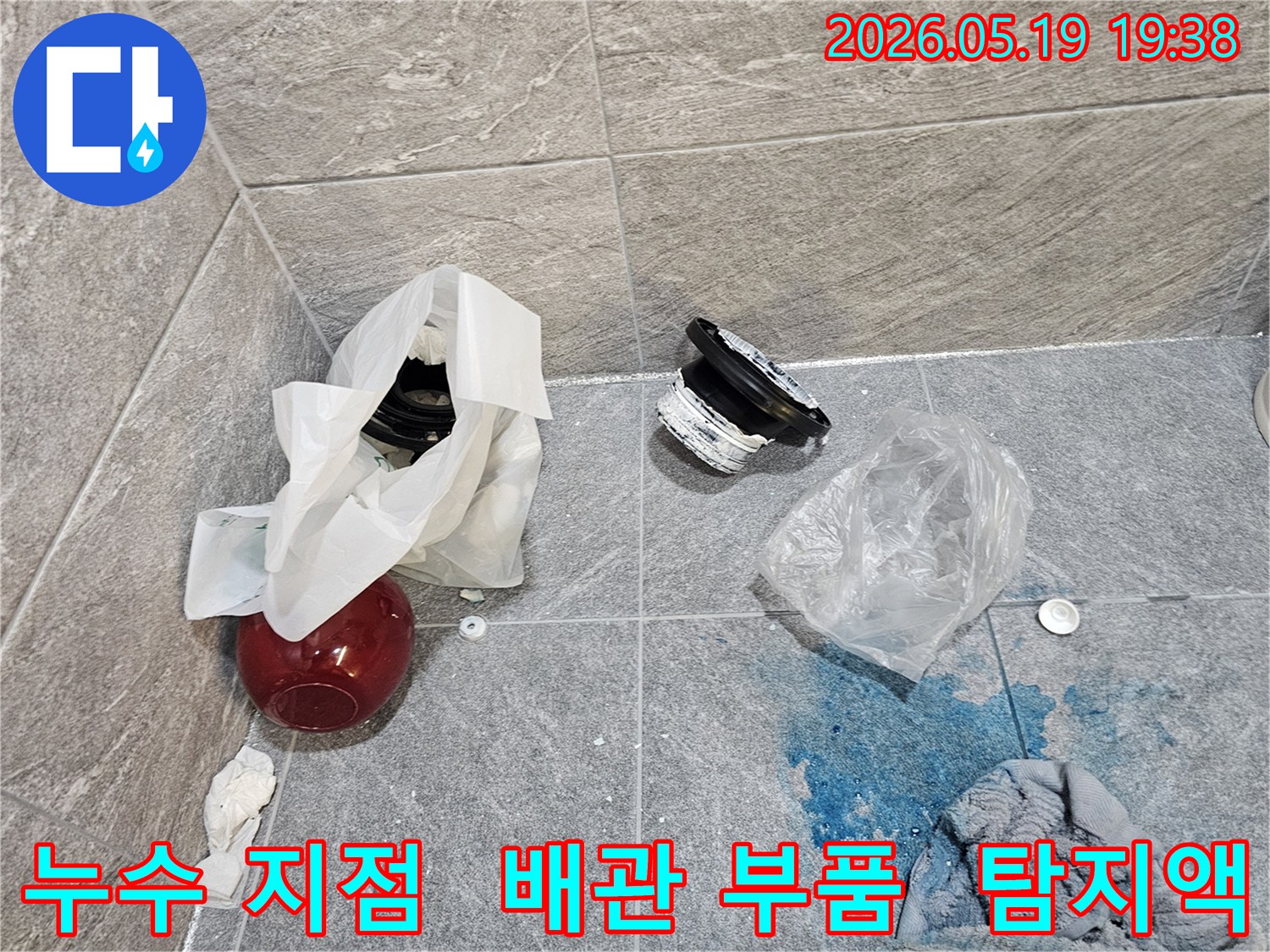 누수 탐지 현장에서-파란색 탐지액으로 확인된 누수 지점과-교체를 위해 해체된 배관 부품들이 바닥에 놓여 있습니다