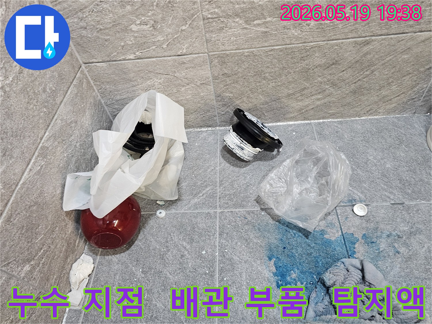 누수 탐지 현장에서-파란색 탐지액으로 확인된 누수 지점과-교체를 위해 해체된 배관 부품들이 바닥에 놓여 있습니다
