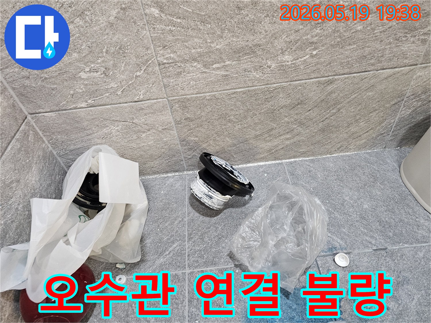 화장실 바닥에 놓인-손상된 오수관 연결 부속과-누수로 인한 푸른색 오염