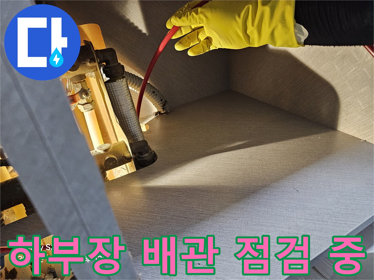 노란색 작업 장갑을 사용해-싱크대 아래쪽 은색 보온재가 감긴-배관을 만져보는 모습