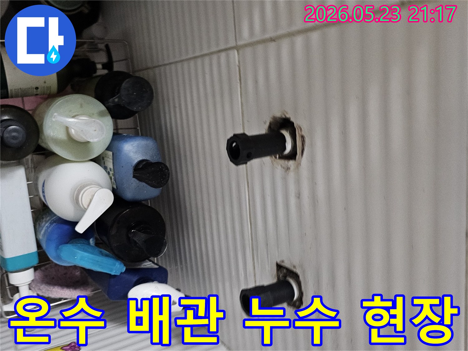 타일 벽면에서 노출된 두 개의 수도 배관 연결 부위를-열화상 탐지 후 온수 배관 누수 여부를-정밀하게 확인하는 장면입니다.