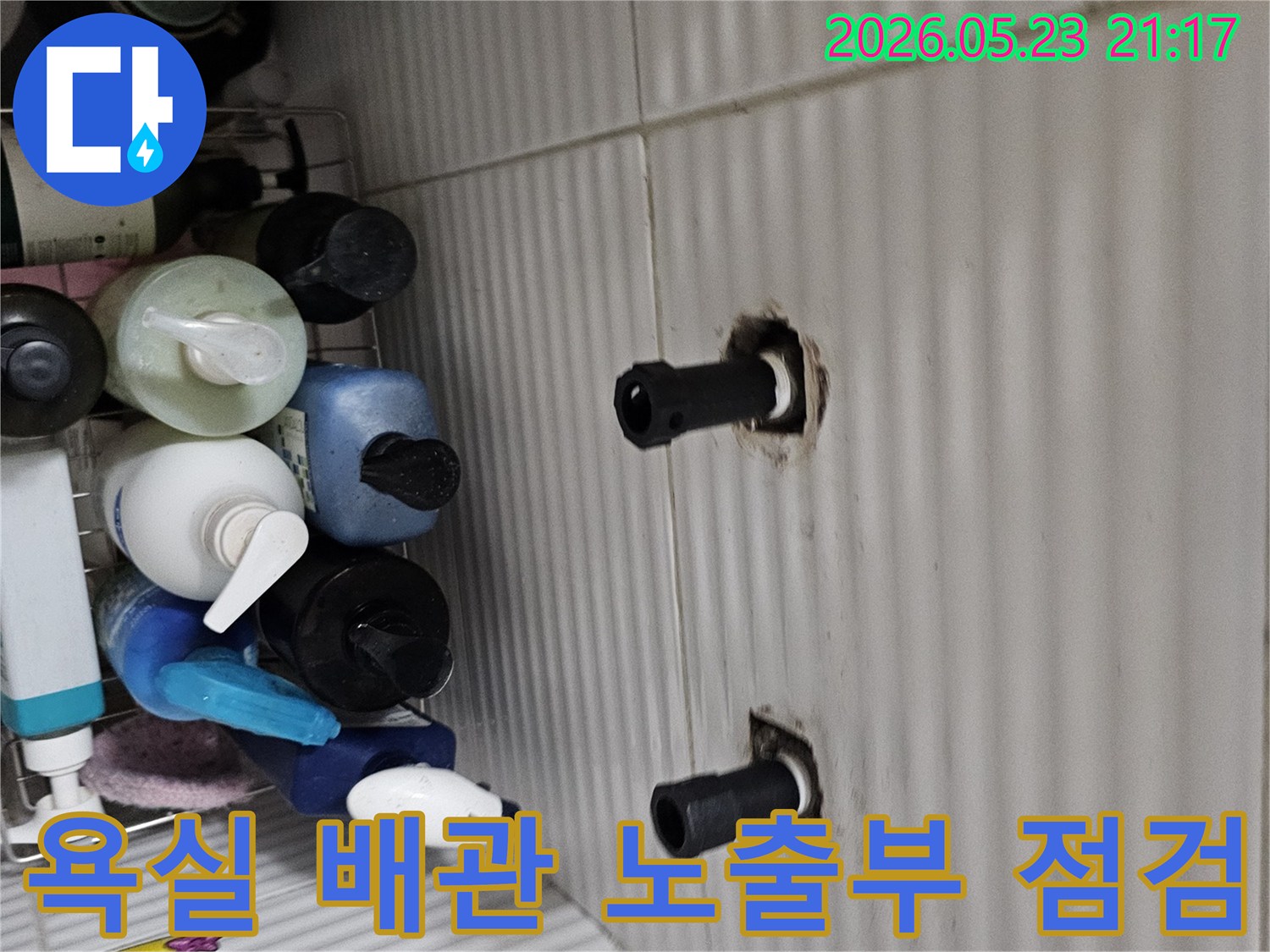 타일 벽면에서 노출된 두 개의 수도 배관 연결부를-누수 여부를 확인하기 위해-정밀하게 점검하는 모습입니다.