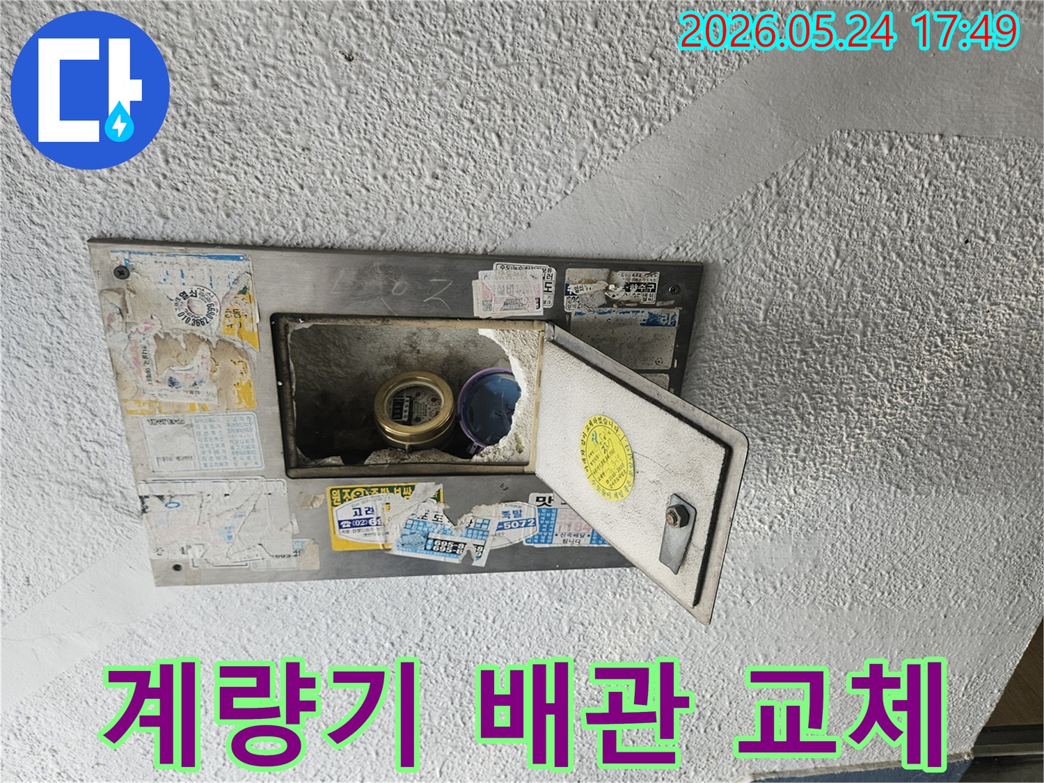 오래된 수도계량기함이 열려있고-내부의 낡은 수도관에서 누수가 발생하여-교체가 필요한 현장 사진입니다.