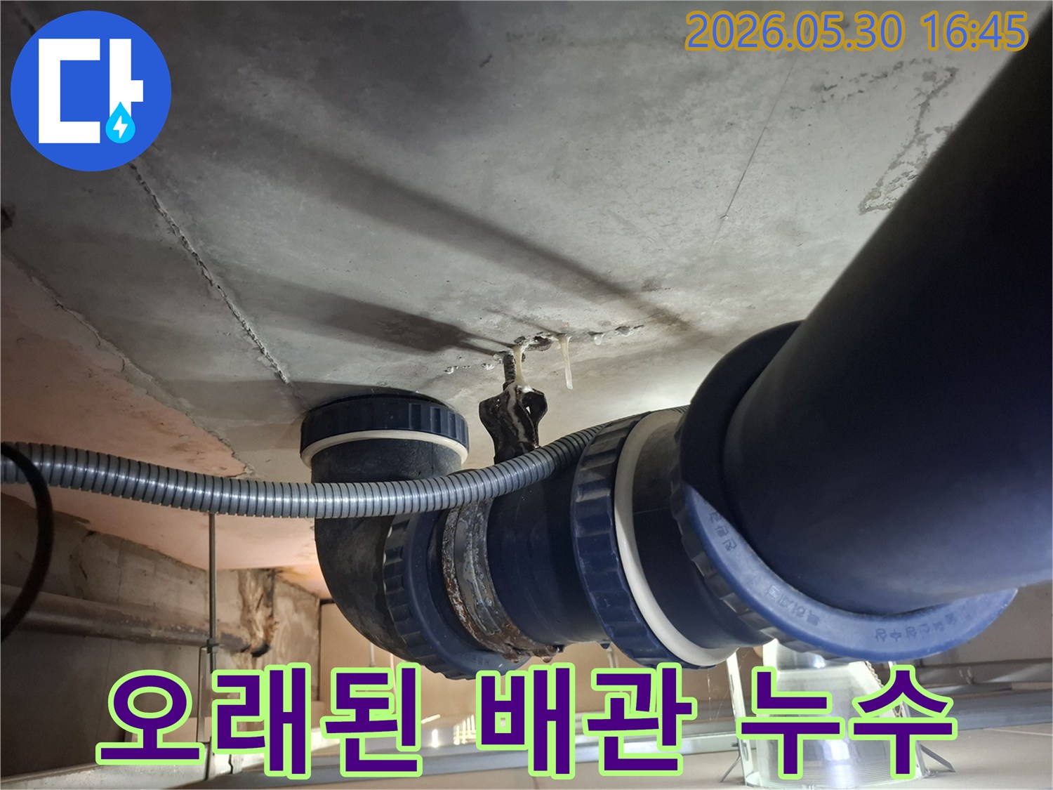 콘크리트 천장 아래-설치된 노후 배관에서-물이 새어 나와-천장에 얼룩을-만드는 모습입니다.