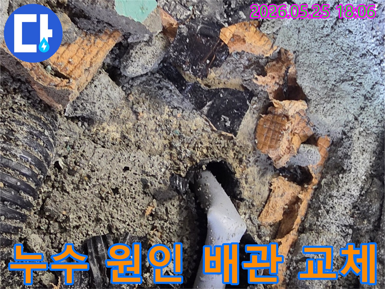 파쇄된 바닥 아래에서 드러난 젖은 배관과 주변의 흙-콘크리트 조각들은-누수 수리를 위한 배관 교체 작업을 보여줍니다.