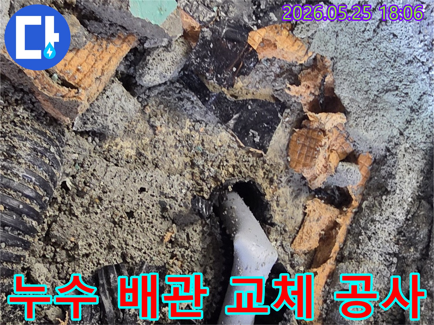 파쇄된 바닥 아래에서 드러난 젖은 배관과 주변의 흙-콘크리트 조각들은-누수 수리를 위한 배관 교체 작업을 보여줍니다.