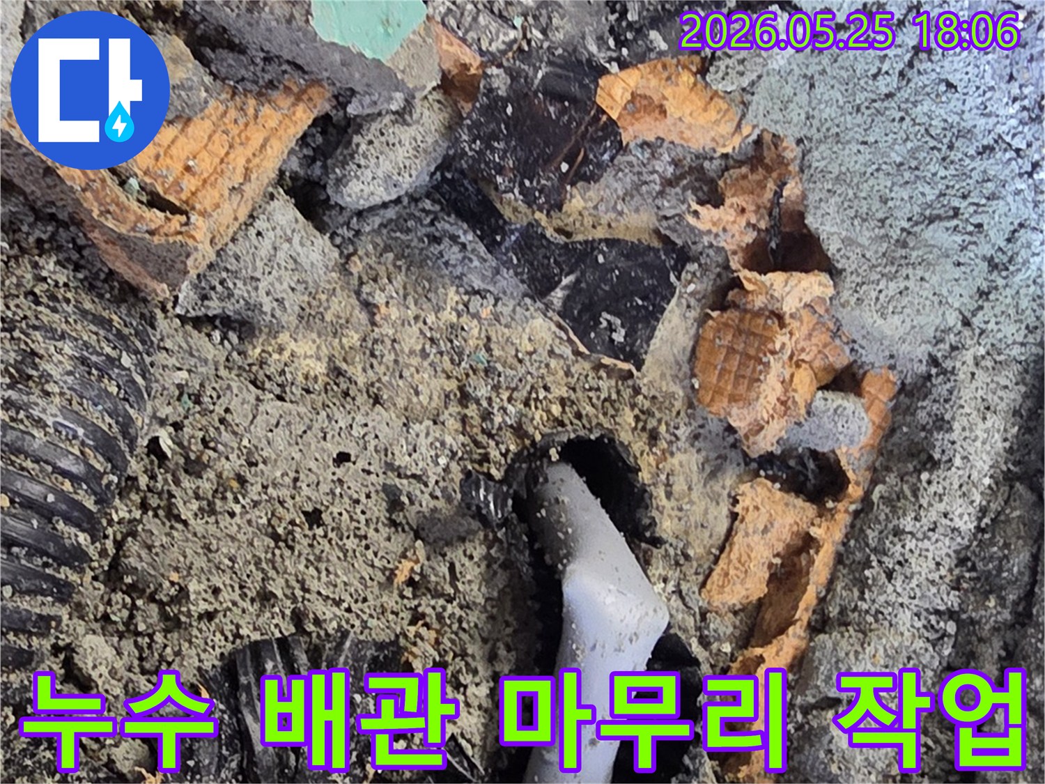 파쇄된 바닥 아래에서 드러난 젖은 배관과 주변의 흙-콘크리트 조각들은-누수 수리를 위한 배관 교체 작업을 보여줍니다.