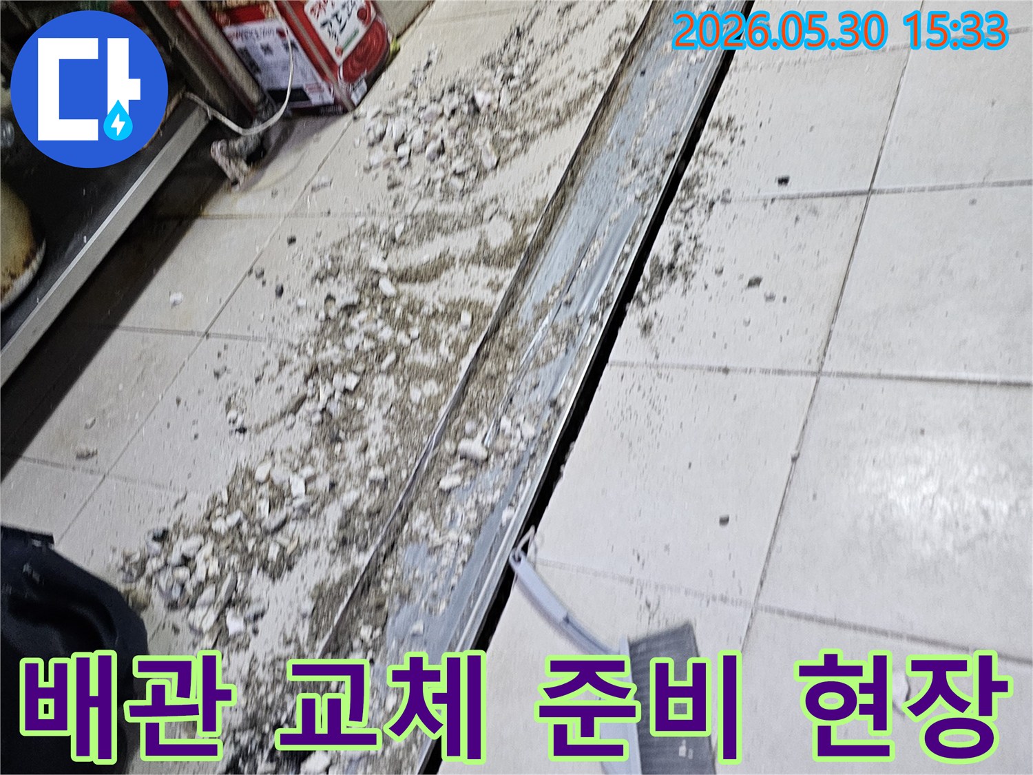 누수 공사 현장에서-바닥 타일 파쇄 후-발생한 잔해물과-청소 도구가-함께 보이는-작업 진행 모습입니다.