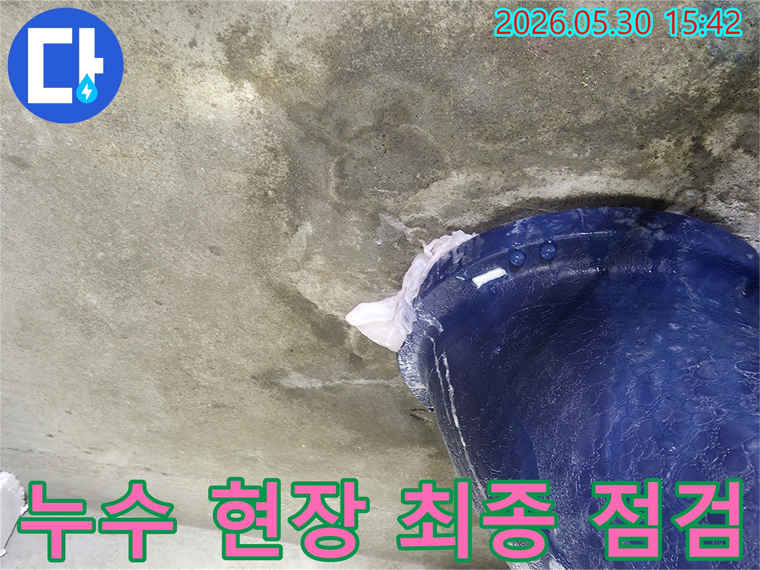 천장에서 물이 떨어지는 누수 현장에서-모든 작업 완료 후-최종 점검을 위해-파란색 양동이로 물을 받아내는 모습입니다.
