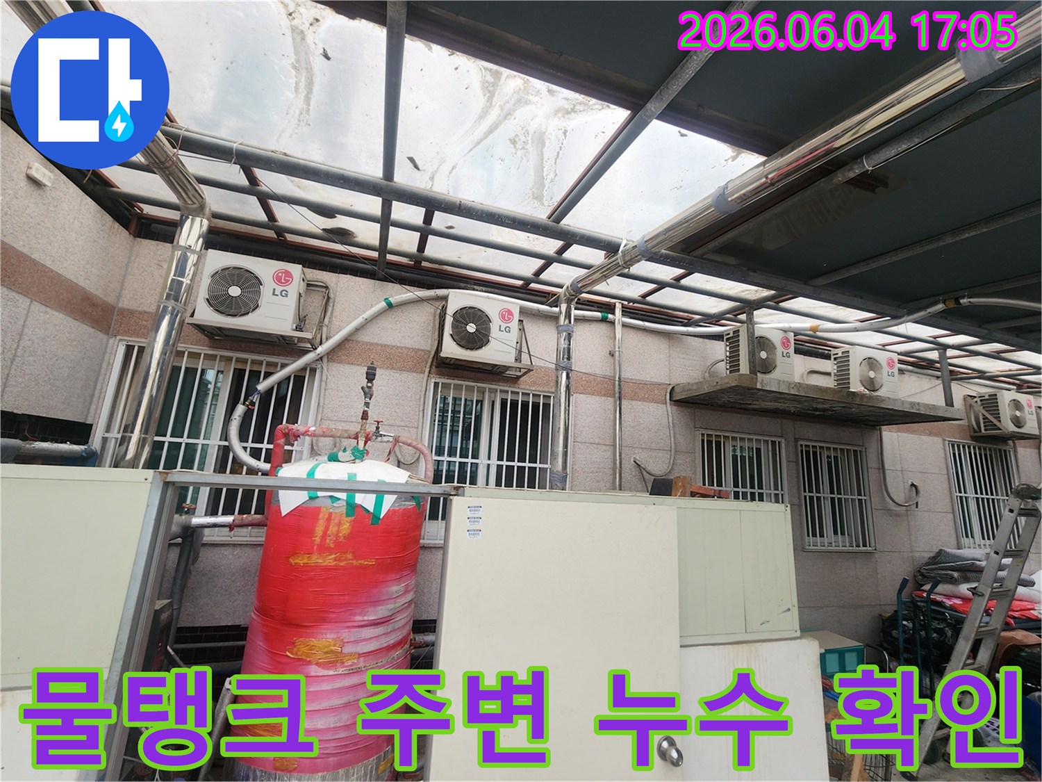 이 사진은 옥상 구조물 아래에 있는-빨간색 대형 물탱크와-그 주변의 배관들을 보여줍니다