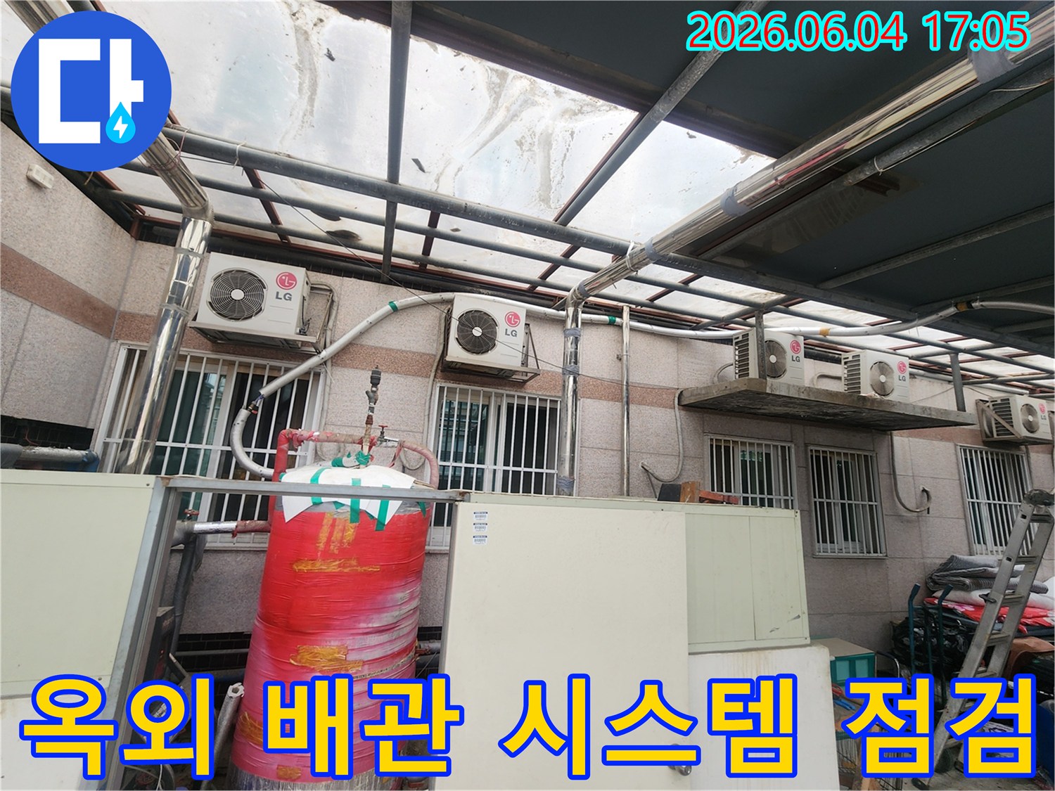 이 이미지는 오래된 건물 외부에 설치된-다양한 배관들과-에어컨 실외기-그리고 물탱크가-복잡하게 얽혀있는 모습을 보여줍니다