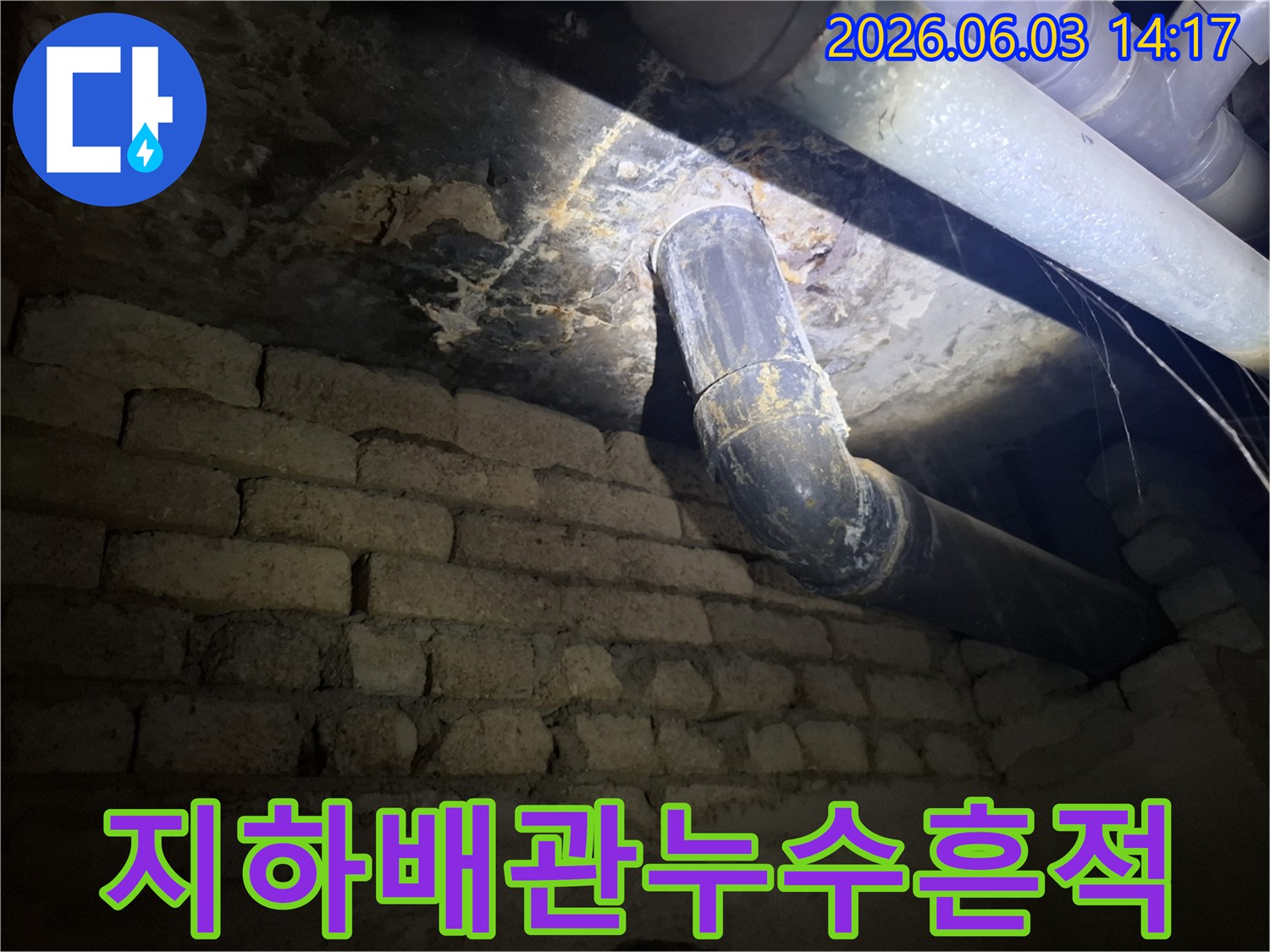 어두운 지하 공간에서-낡은 배관과-벽돌 벽에 발생한-누수 흔적을-조명으로 비춰-면밀히 조사하는 모습
