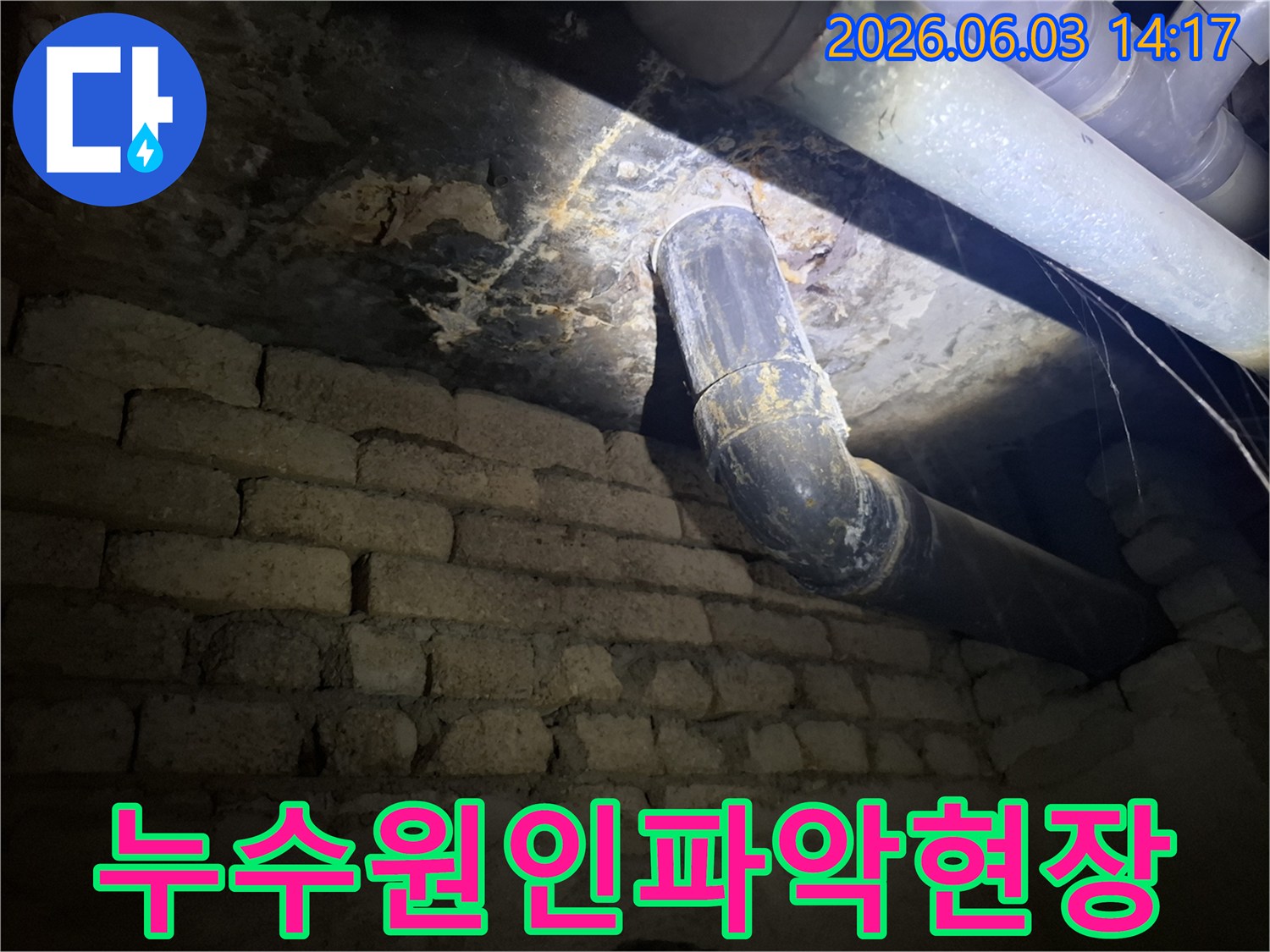 어두운 지하 공간에서-낡은 배관과-벽돌 벽에 발생한-누수 흔적을-조명으로 비춰-정밀하게 확인하는 모습