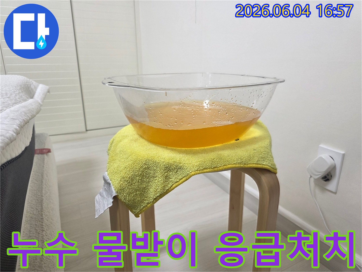 천장 누수 발생 시-추가적인 물 피해를 막기 위해-설치된 임시 물받이와-그 아래 노란 수건의 모습
