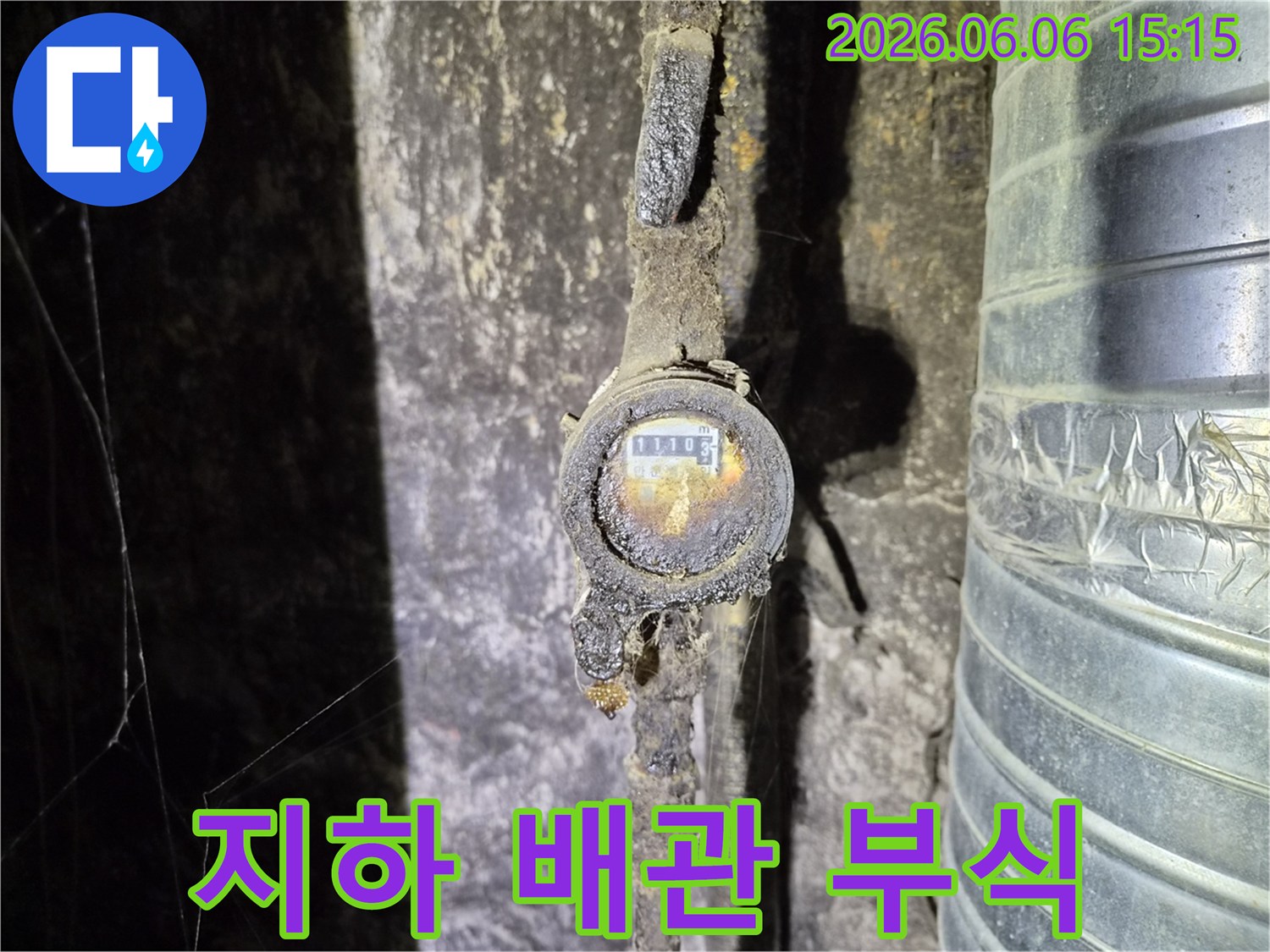 어둡고 습한 지하 공간에서 발견된-오래된 수도 계량기와 심하게 부식된 배관으로-누수 발생의 직접적인 원인을 보여줍니다
