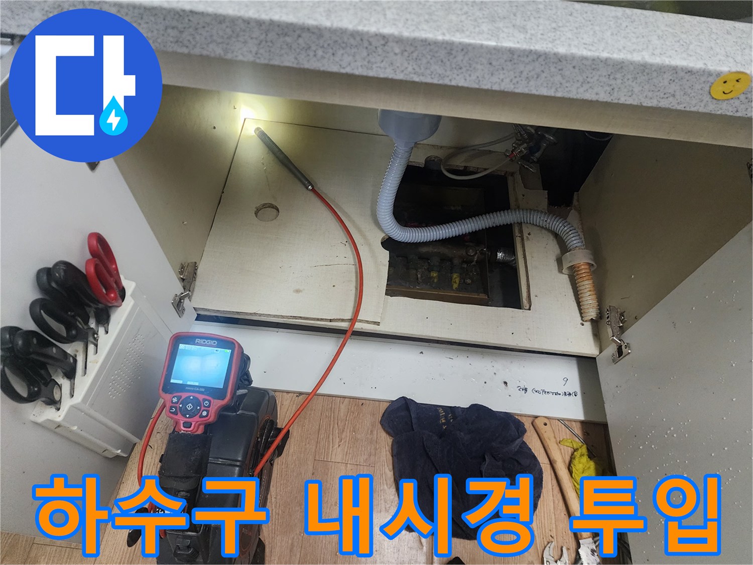 주방 싱크대 하부장 아래에서 배관 내부를 촬영하기 위해 내시경 선을 연결한 모습입니다.