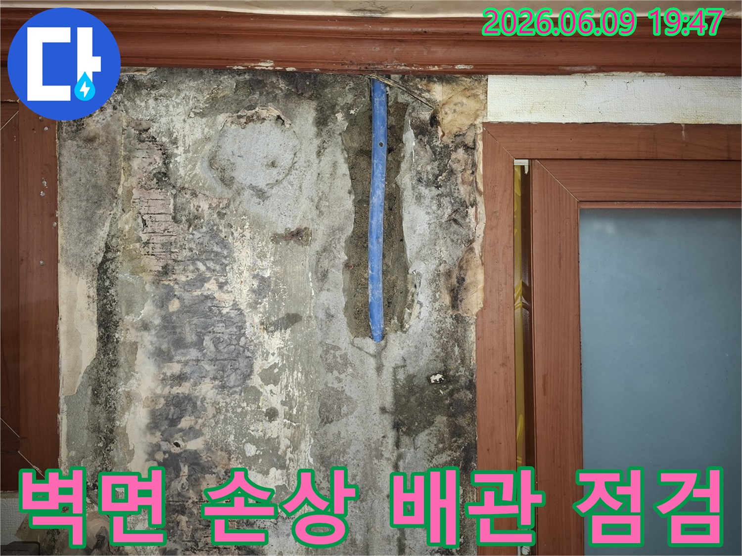 수도배관-누수로-인해-벽면이-심하게-손상되고-배관이-노출된-현장을-점검하는-사진