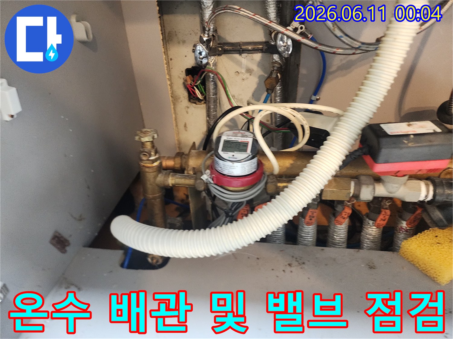 금속 소재의 온수 공급 밸브와 연결된 흰색 주름관이 보이는 배관 내부 모습입니다.