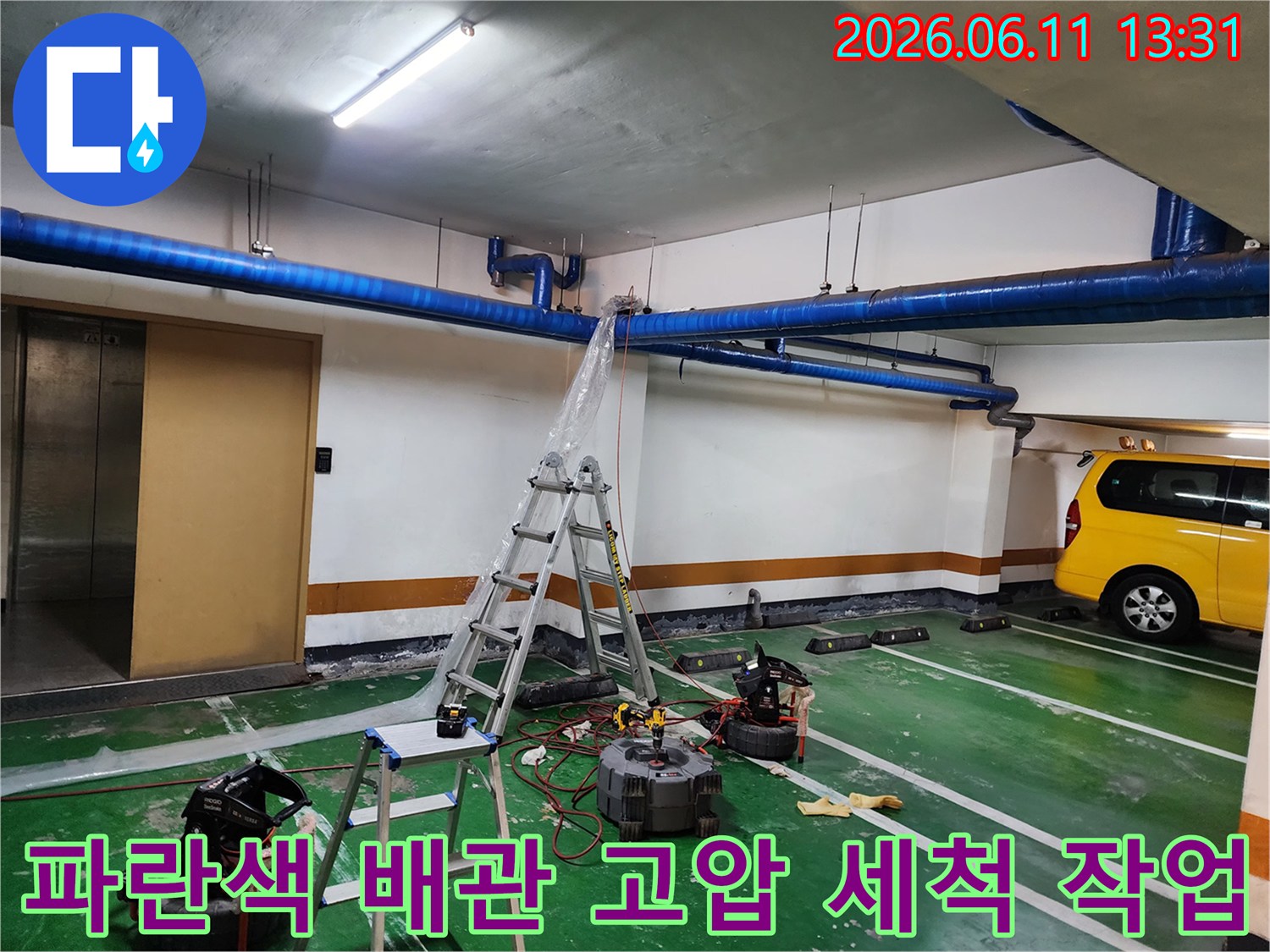 지하주차장 천장의 파란색 대형 배관을 고압 세척기로 청소하는 현장 사진입니다.