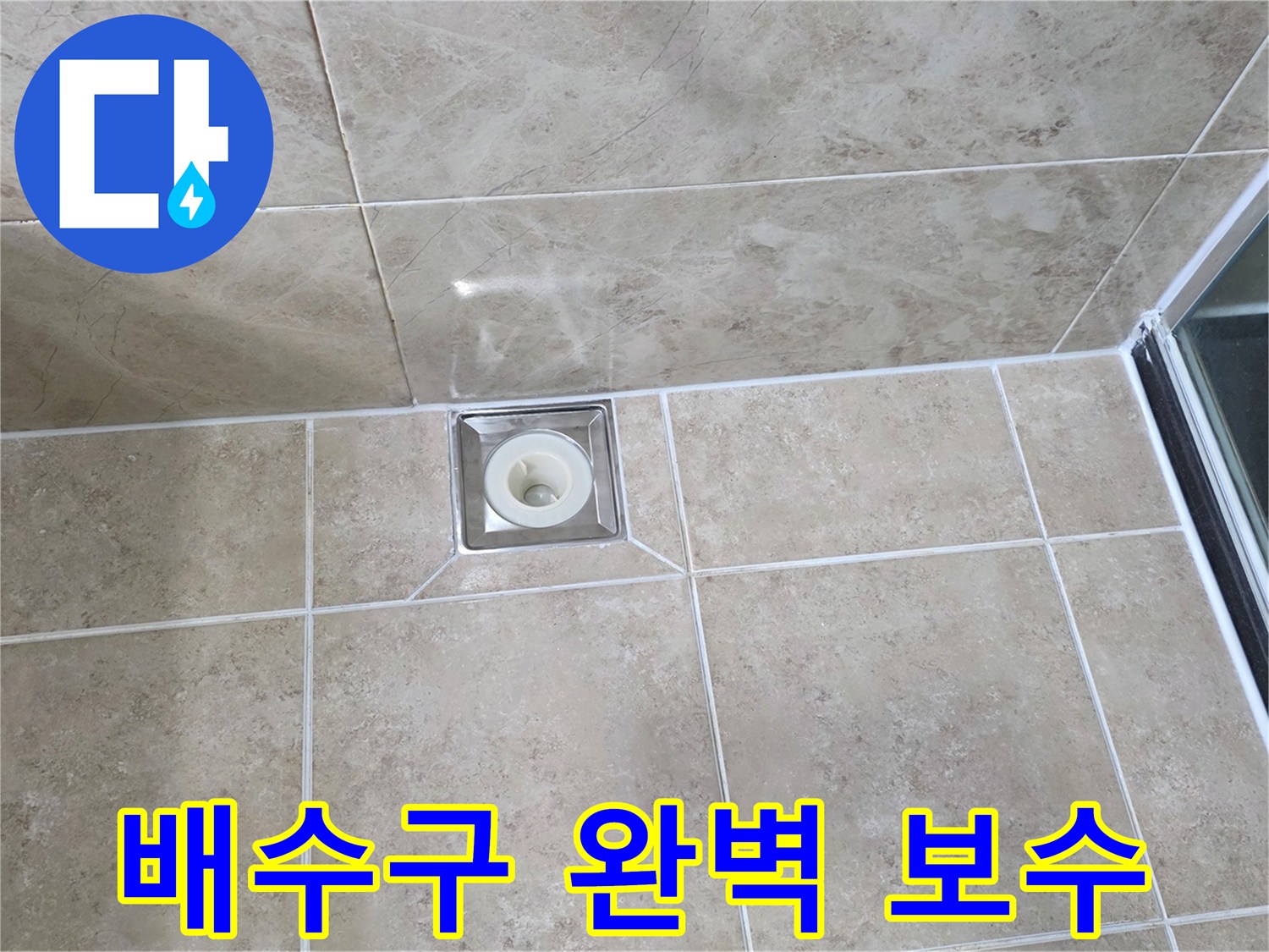 베이지색 타일 바닥에 설치된-금속 사각 배수구의 모습으로-주변 타일과 줄눈의 마감 상태를 보여줍니다