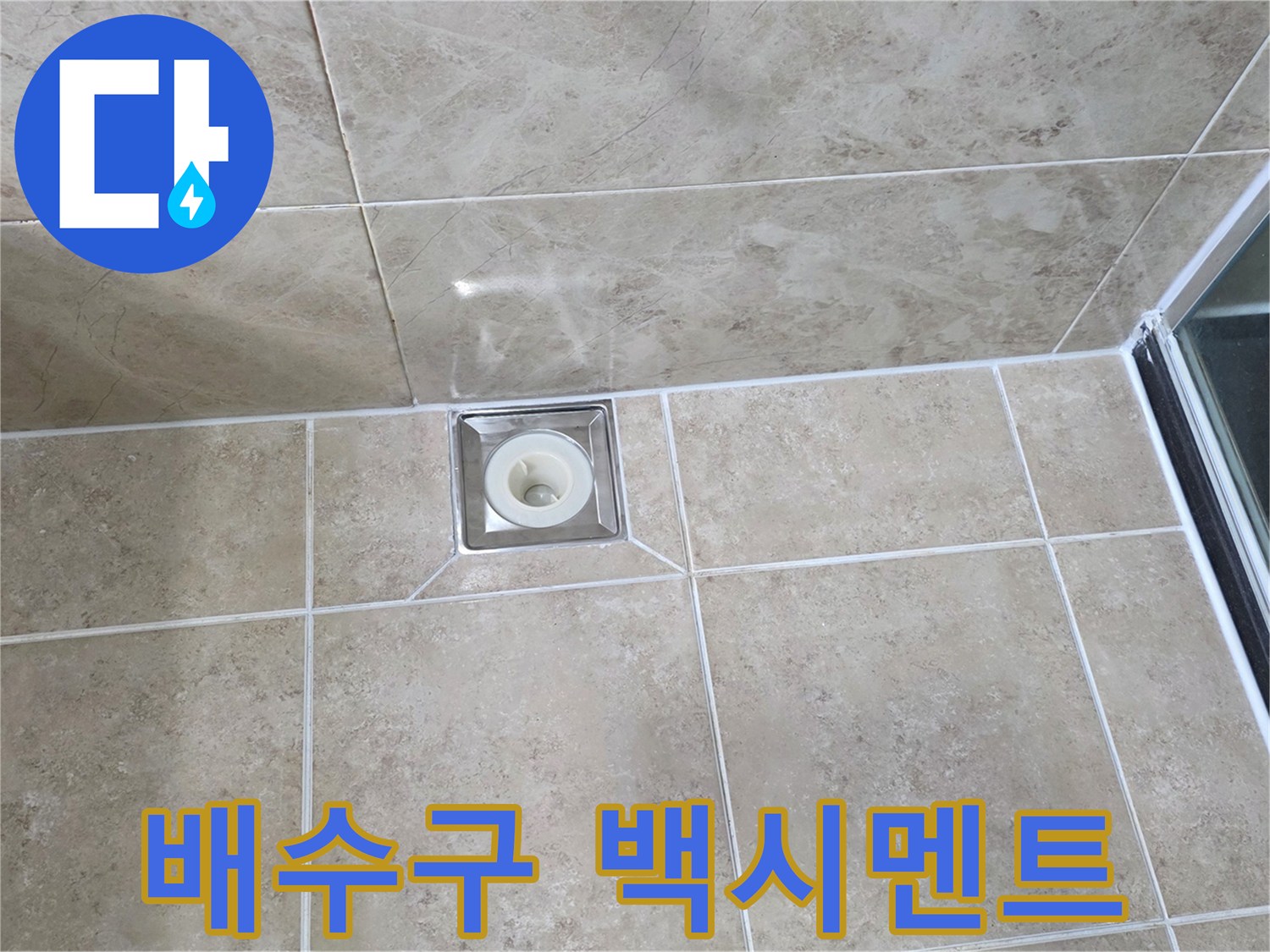 베이지색 타일 바닥에 설치된-사각형 금속 배수구의 모습으로-주변 백시멘트의 마감 상태를 보여줍니다