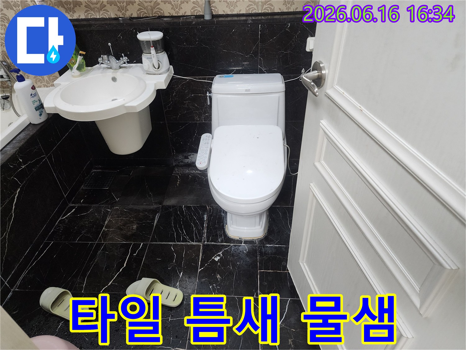 검은색 대리석 무늬 타일 바닥에-하얀색 변기가 놓여있고-그 주변 타일 틈새로-물이 새어 나와 생긴-하얀 침전물이 보이는-욕실 사진입니다.
