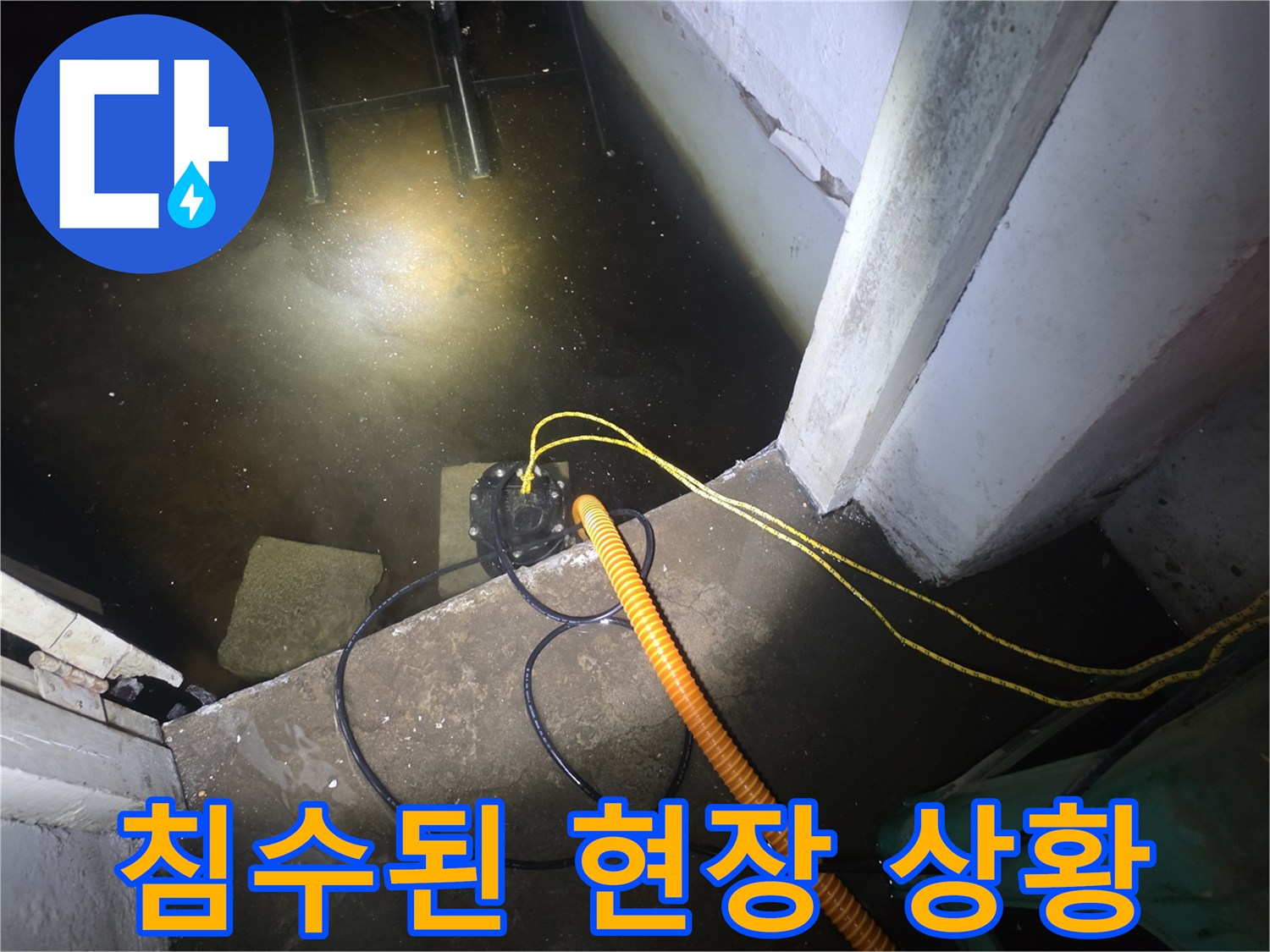 어두운 지하실 바닥에 물이 차 있고 배수 장비가 놓여 있음