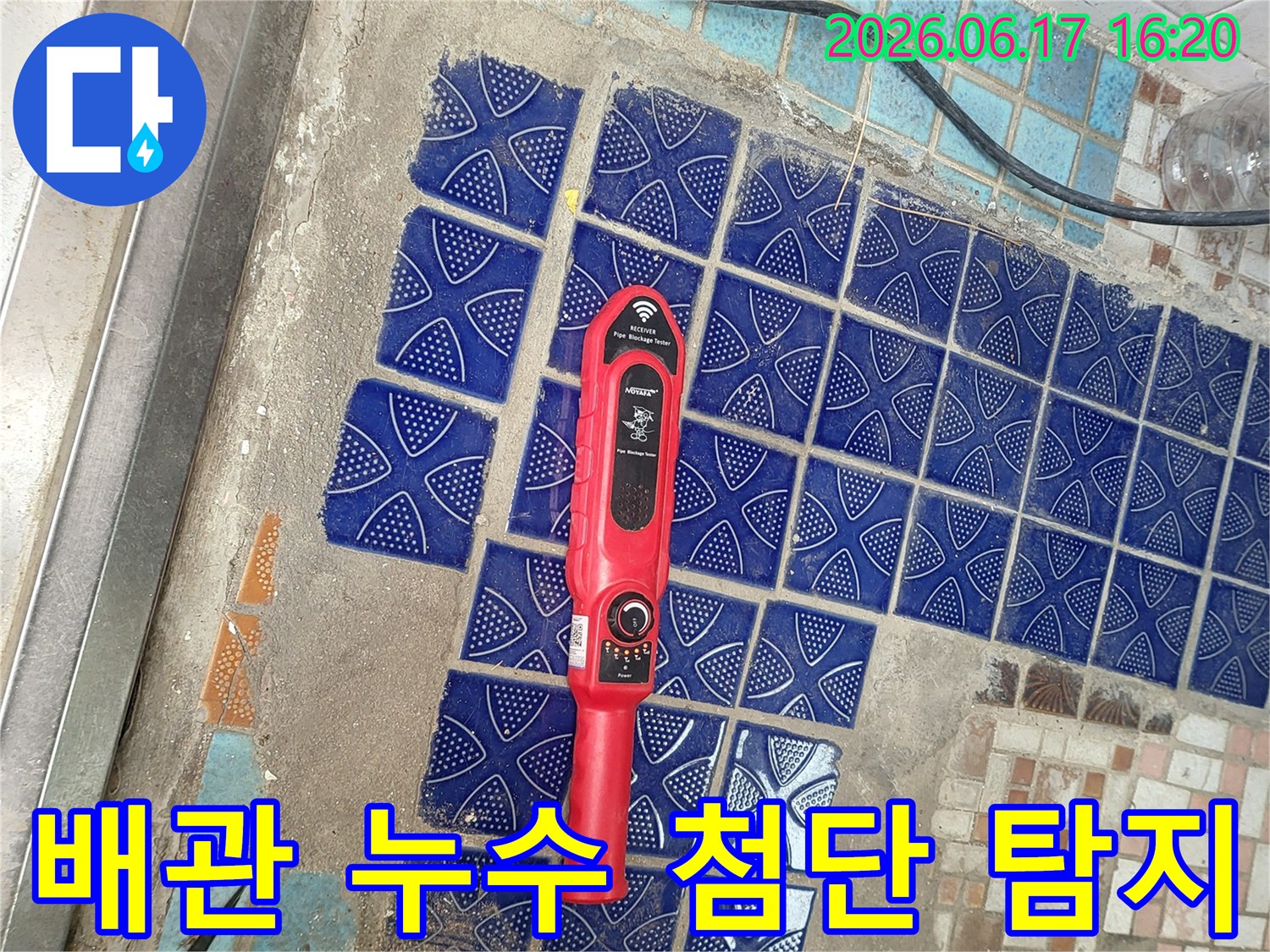 파란색 타일이 부분적으로 제거된 욕실 바닥에-붉은색 첨단 누수탐지 장비가 놓여-배관 누수 지점을 정확히 찾는 모습