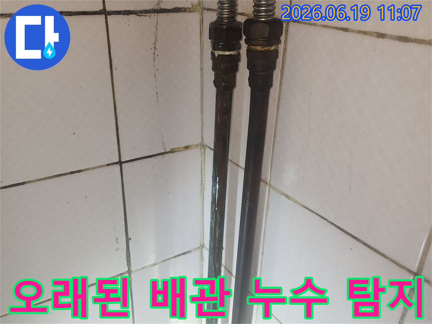 오래된 배관의 연결 부위와 주변 타일의 상태를 보여주며-누수 탐지 과정의 일부입니다