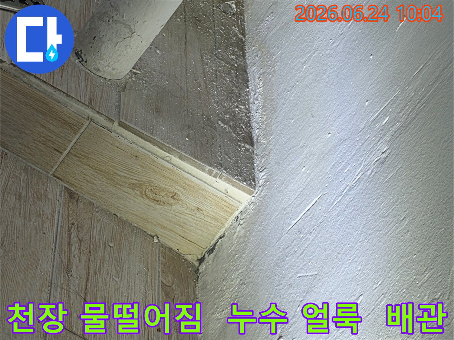 천장 모서리에서-물방울이 떨어지면서-생긴 누수 얼룩과-배관 주변의-젖은 흔적을-보여주는 사진