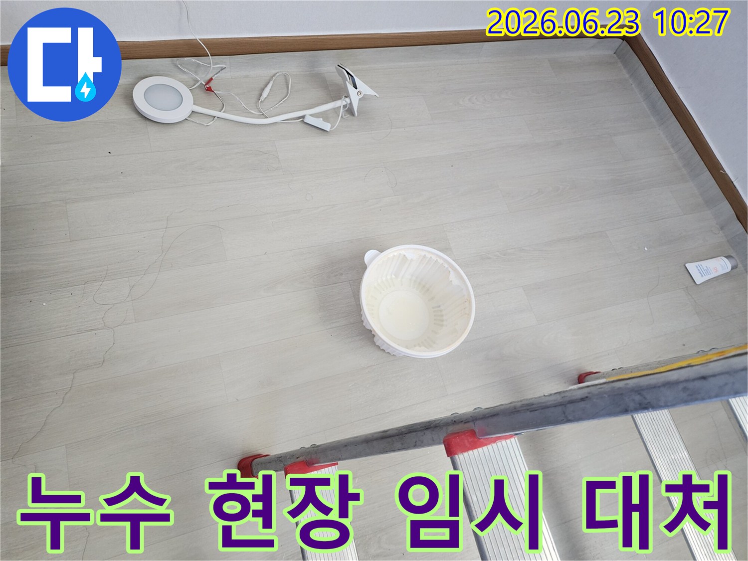 누수로 인해 바닥에 물이 떨어지는 것을 임시로 받는 그릇과-누수 지점 확인을 위한 사다리-작업용 조명 장비가 바닥에 놓여 있는-누수 공사 전 현장 모습입니다