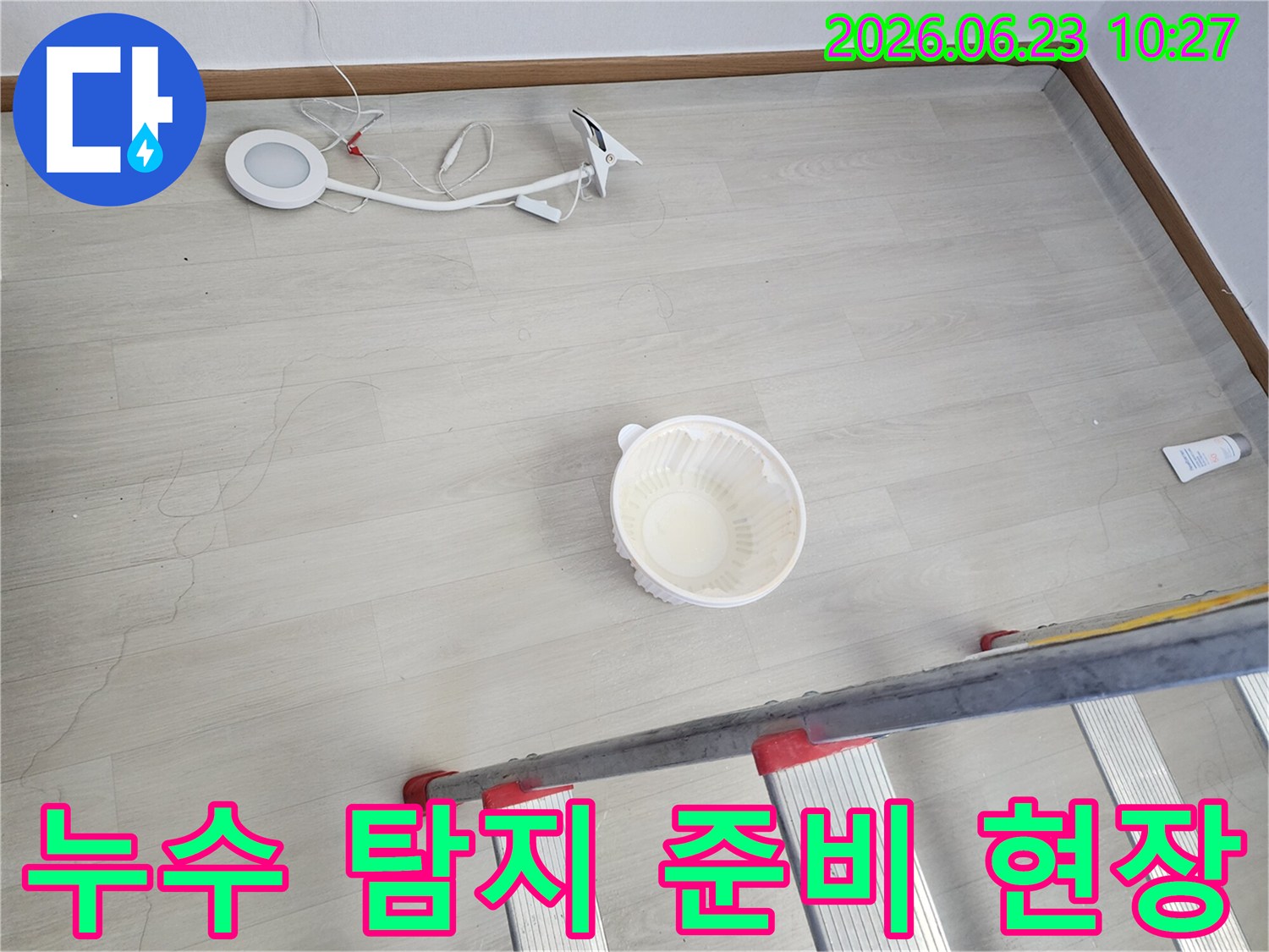 천장에서 떨어지는 물을 임시로 받는 그릇과-누수 지점 확인을 위한 사다리-정밀 탐지를 위한 조명 장비가 바닥에 놓여 있는-누수 공사 전 준비 모습입니다