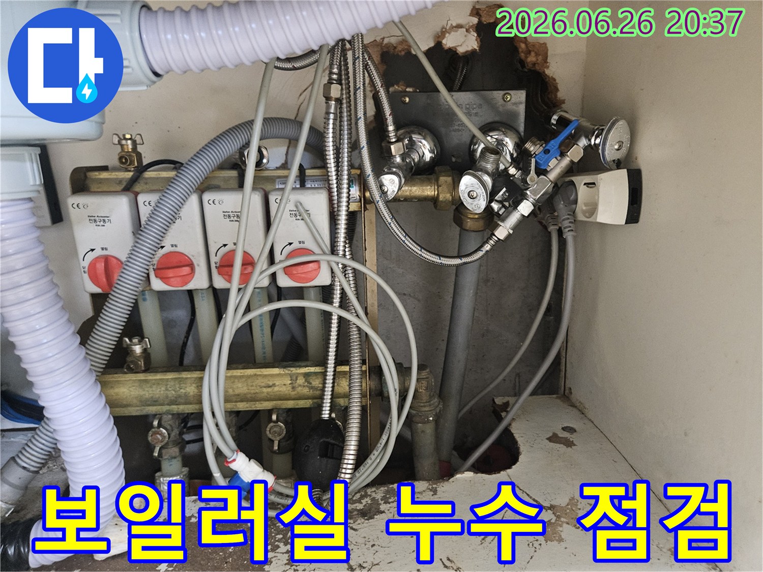이 이미지는-아파트 보일러실의-복잡한 배관과-밸브-그리고-전기 콘센트가-보이는-누수 현장의-전반적인 모습을-제공합니다