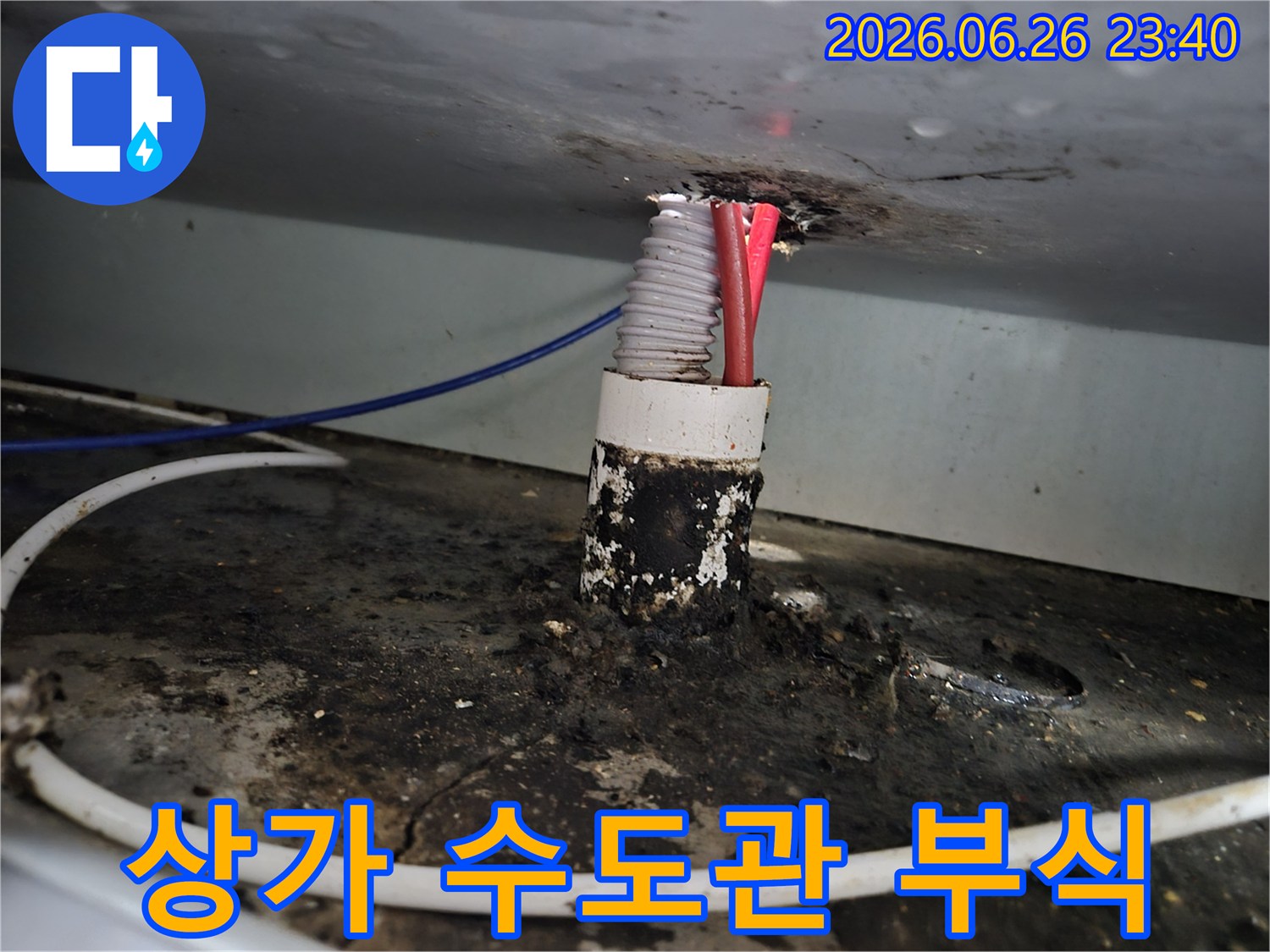 상가 건물 내부의 오래된 수도관 배관 틈새에서-발생한 심각한 부식과 누수 흔적을 보여줍니다.