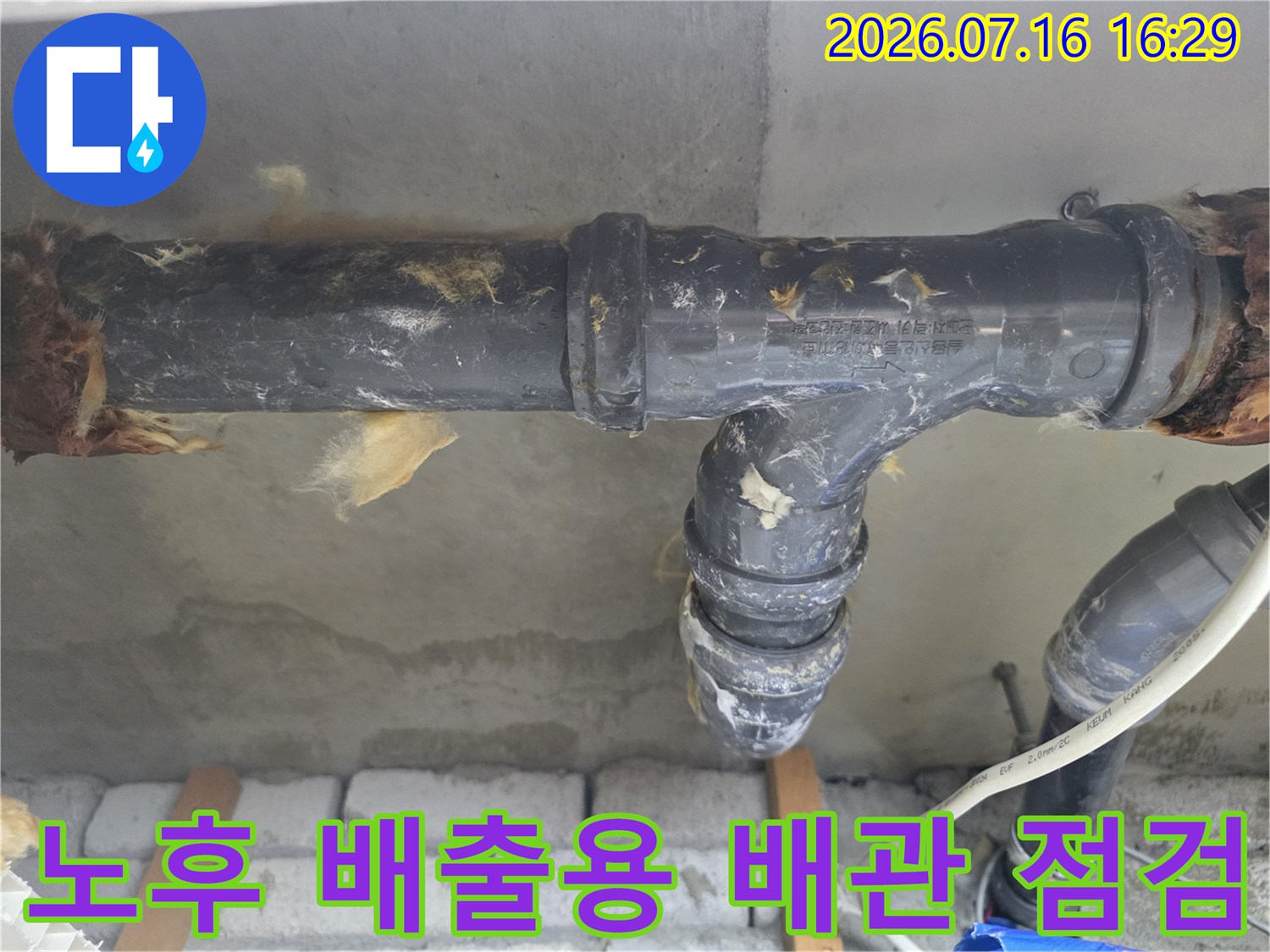 천장 안쪽의 노란색 단열재와 검은색 배수 파이프가 있는 공간을 진단하는 모습