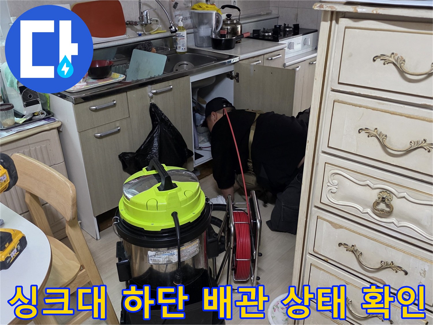 작업자가 싱크대 하부장을 열고 배수 호스 연결부를 점검하는 장면