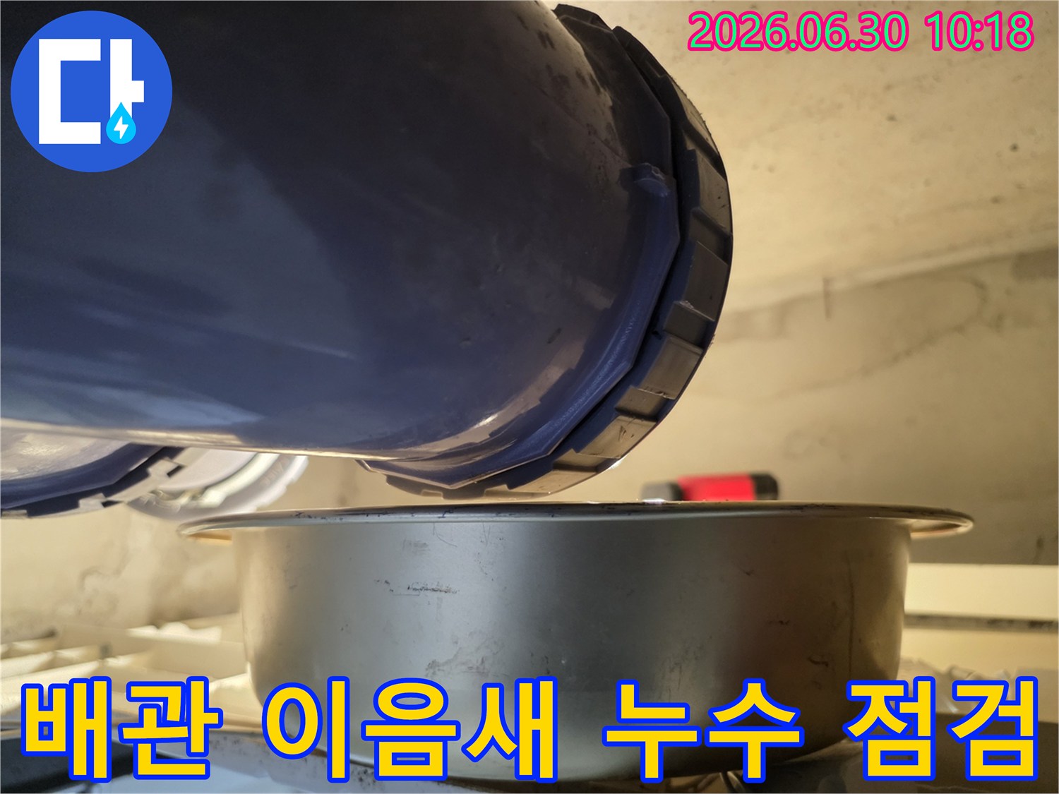누수-현장에서-배관의-이음새-부분에서-물이-새는-것을-발견하고-아래에-물받이를-놓아-정밀하게-점검하고-있는-사진입니다.