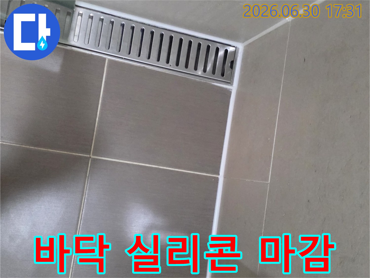 화장실 바닥의-타일 이음새와-선형 배수구 주변에-새롭게 시공된-하얀색-실리콘 마감 상태를-자세히 보여줍니다.