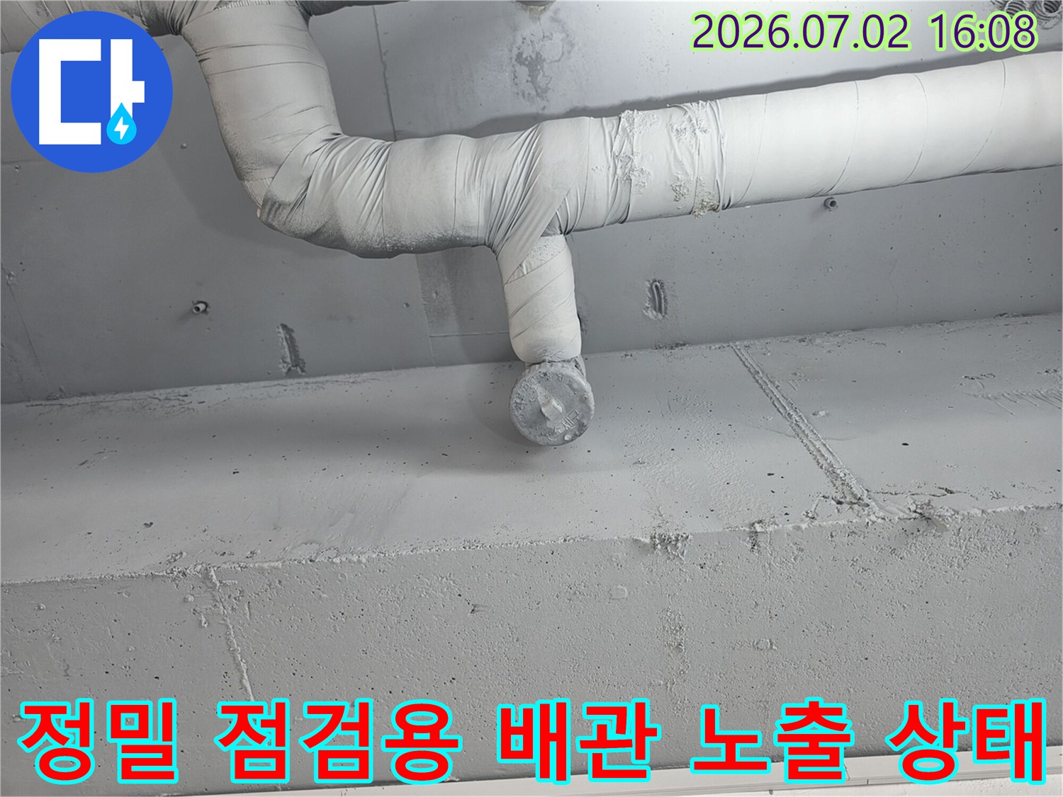 흰색 보온재를 제거하고 노출된 수직 및 수평 배관의 연결부 세부 확인 장면