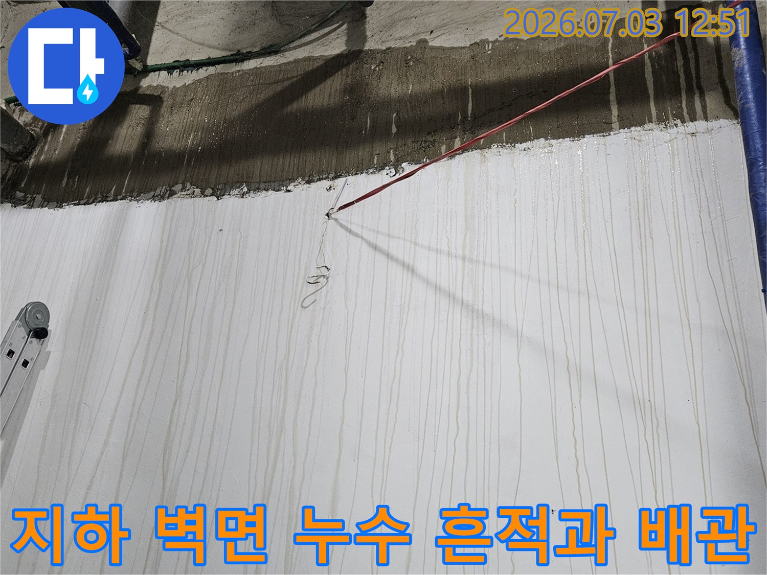 지하 공간의 파란색 보온재 배관과 물줄기 자국이 남은 흰색 벽면-사다리가 세워져 있는 모습
