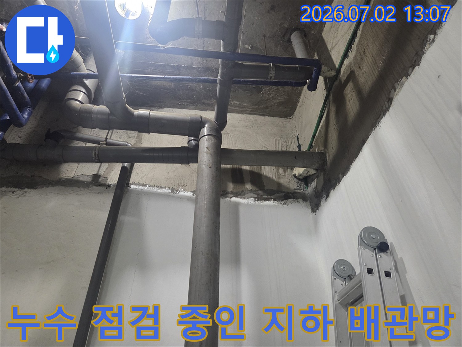 회색빛의 굵은 하수 배관이 수직과 수평으로 교차하며 설치된 지하 천장-벽면 구조물