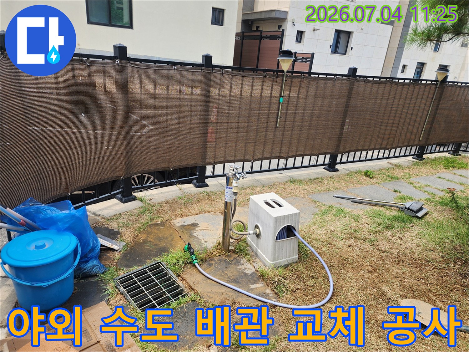 마당에 설치된 수조형 장치와 연결된 파란색 호스의 수도 배관 보수 모습