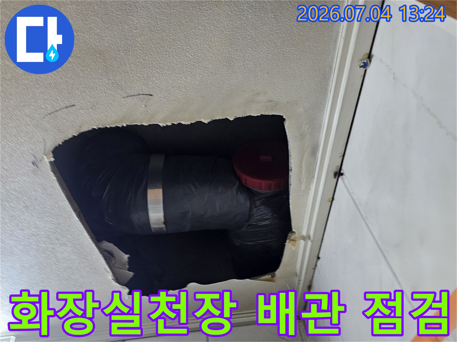 화장실 천장 내부를 확인하기 위해 타공된 구멍을 통해 노출된 검은색 단열재로 감싸진 배관의 모습