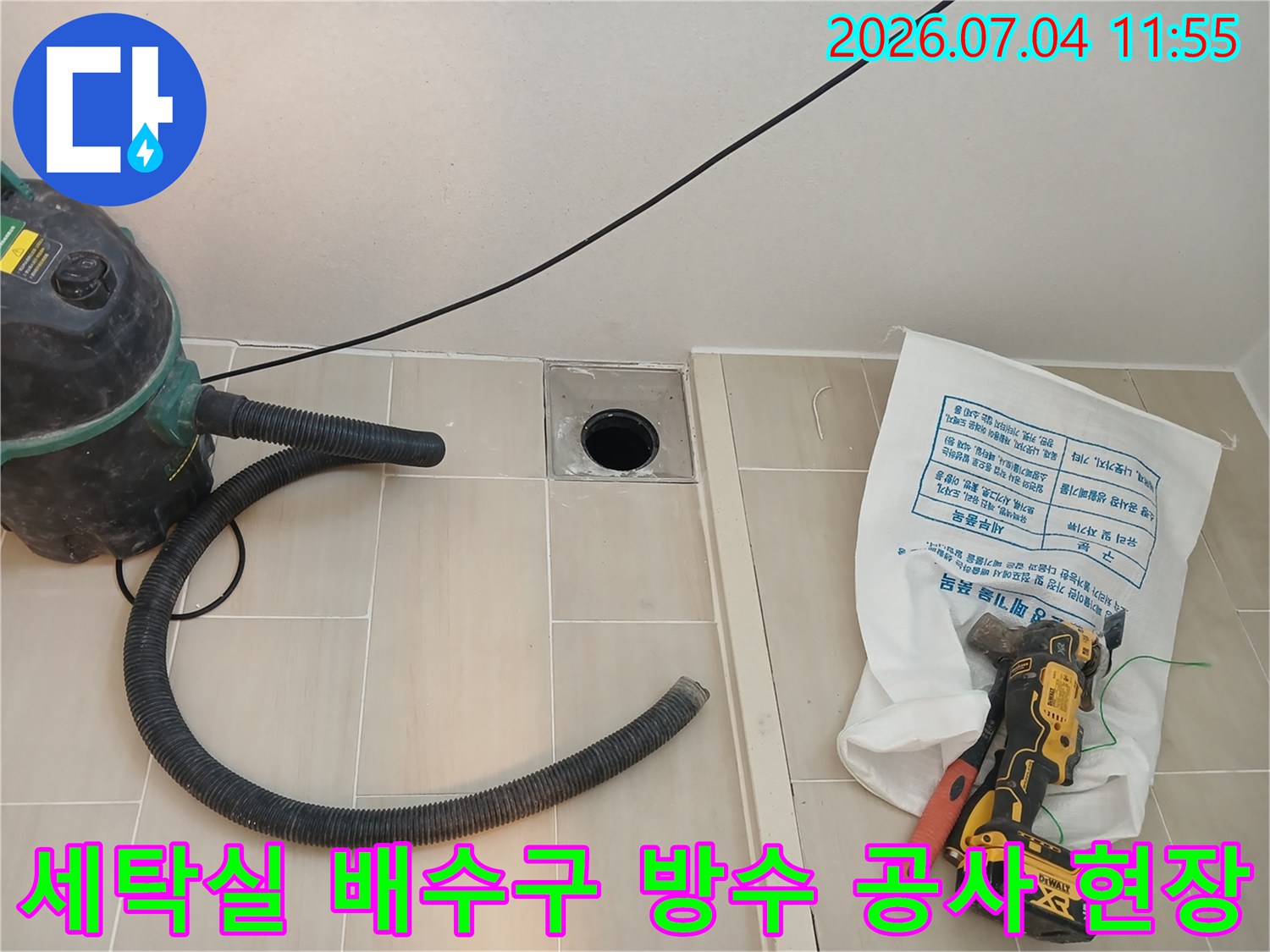 먼지 제거 장비와 드릴을 갖추고 세탁실 배수구 주변을 정밀 점검하는 모습