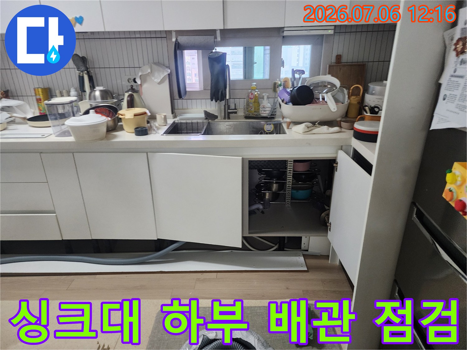 싱크대 아래를 노출하여 배수 호스 연결 상태와 주변 환경을 진단하는 현장 모습